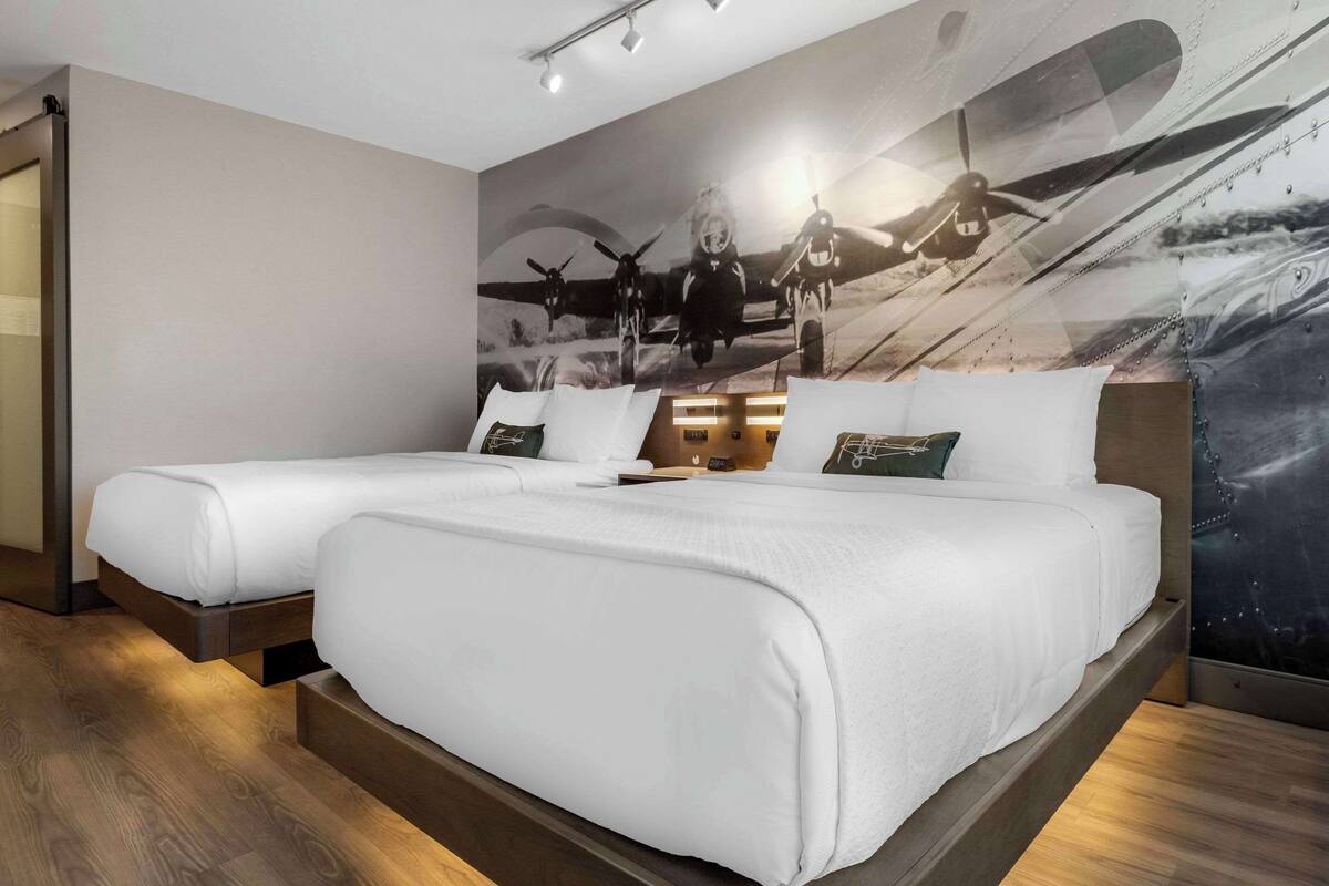 A hotel room with two beds, a large mural of vintage aircraft on the wall, and a wooden floor.