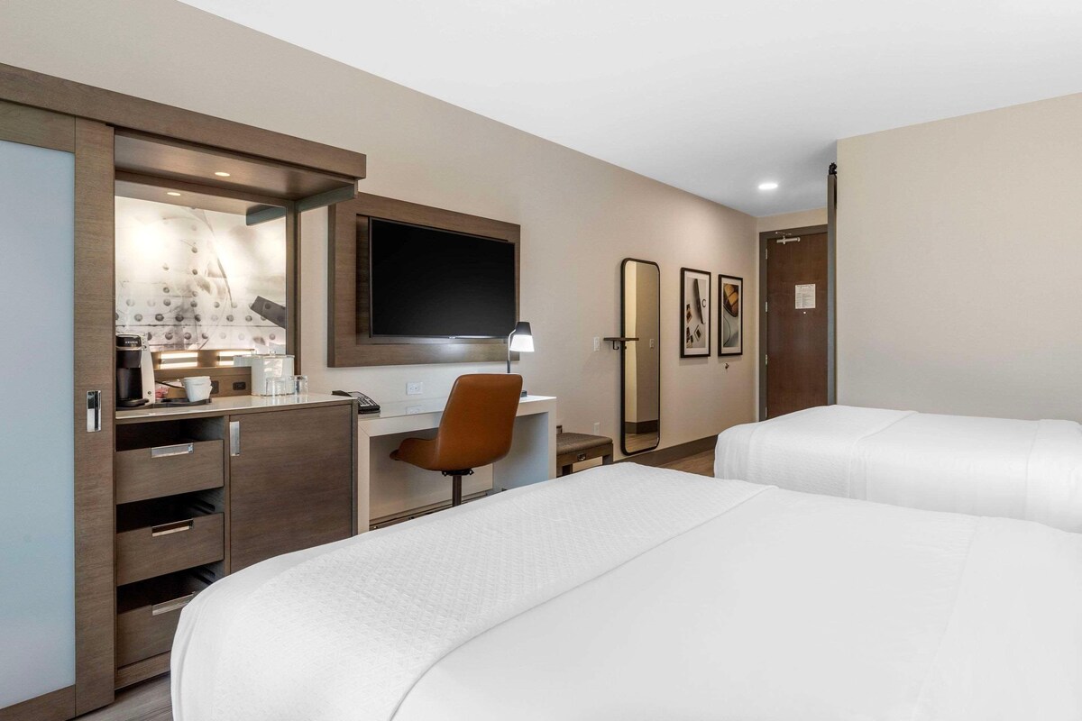 Una habitación de hotel con dos camas, un escritorio, una silla, un televisor y un minibar.