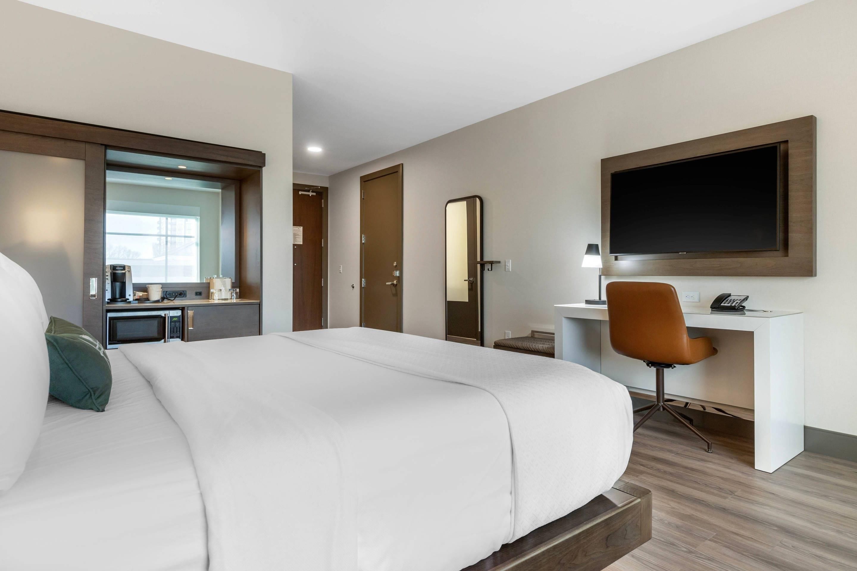 Una habitación de hotel con una cama grande, un escritorio con una silla, un televisor de pantalla plana y una cafetera.