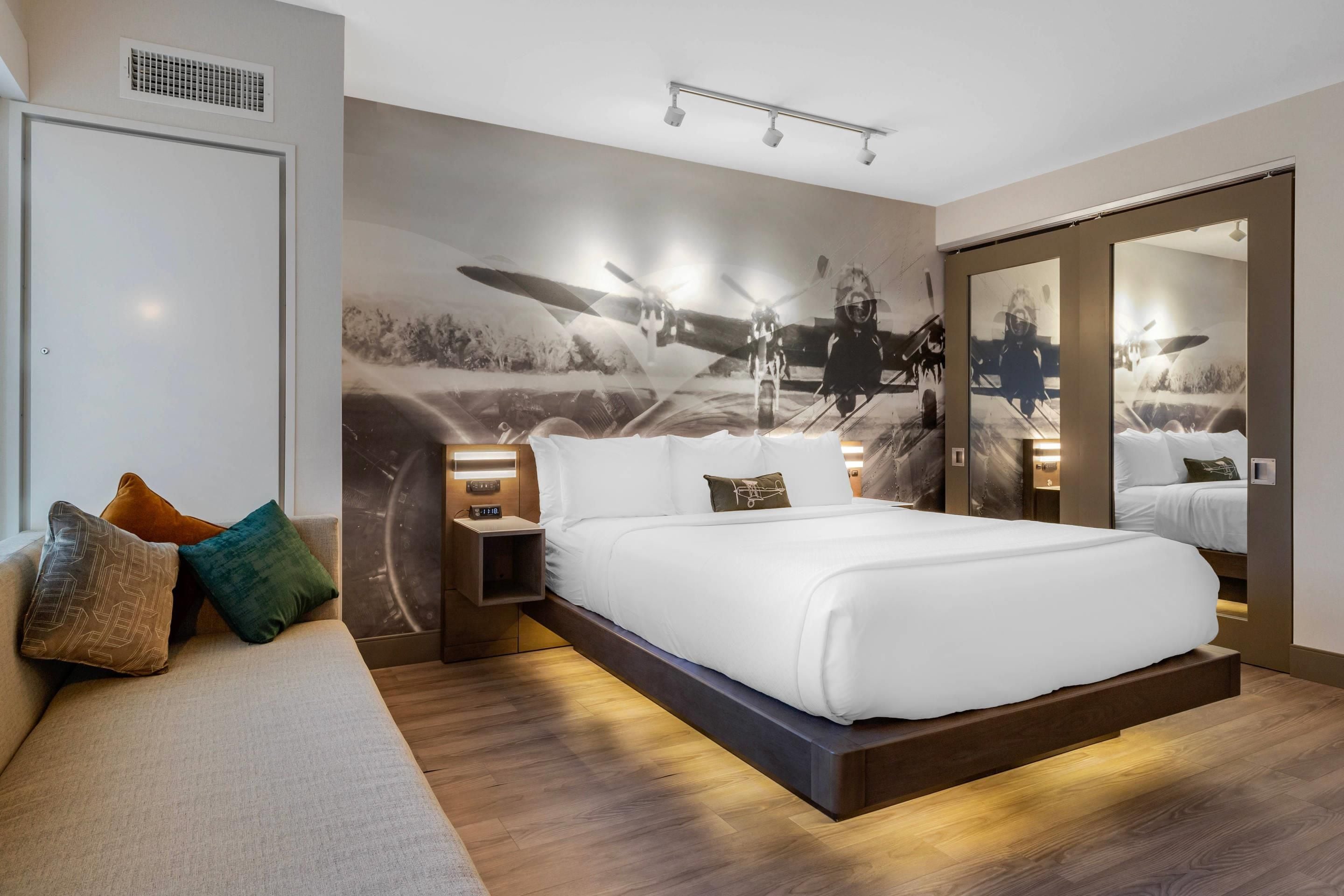 Een moderne slaapkamer met een groot bed, nachtkastjes, een nachtlampje, een spiegel aan de muur en een plafondlamp.