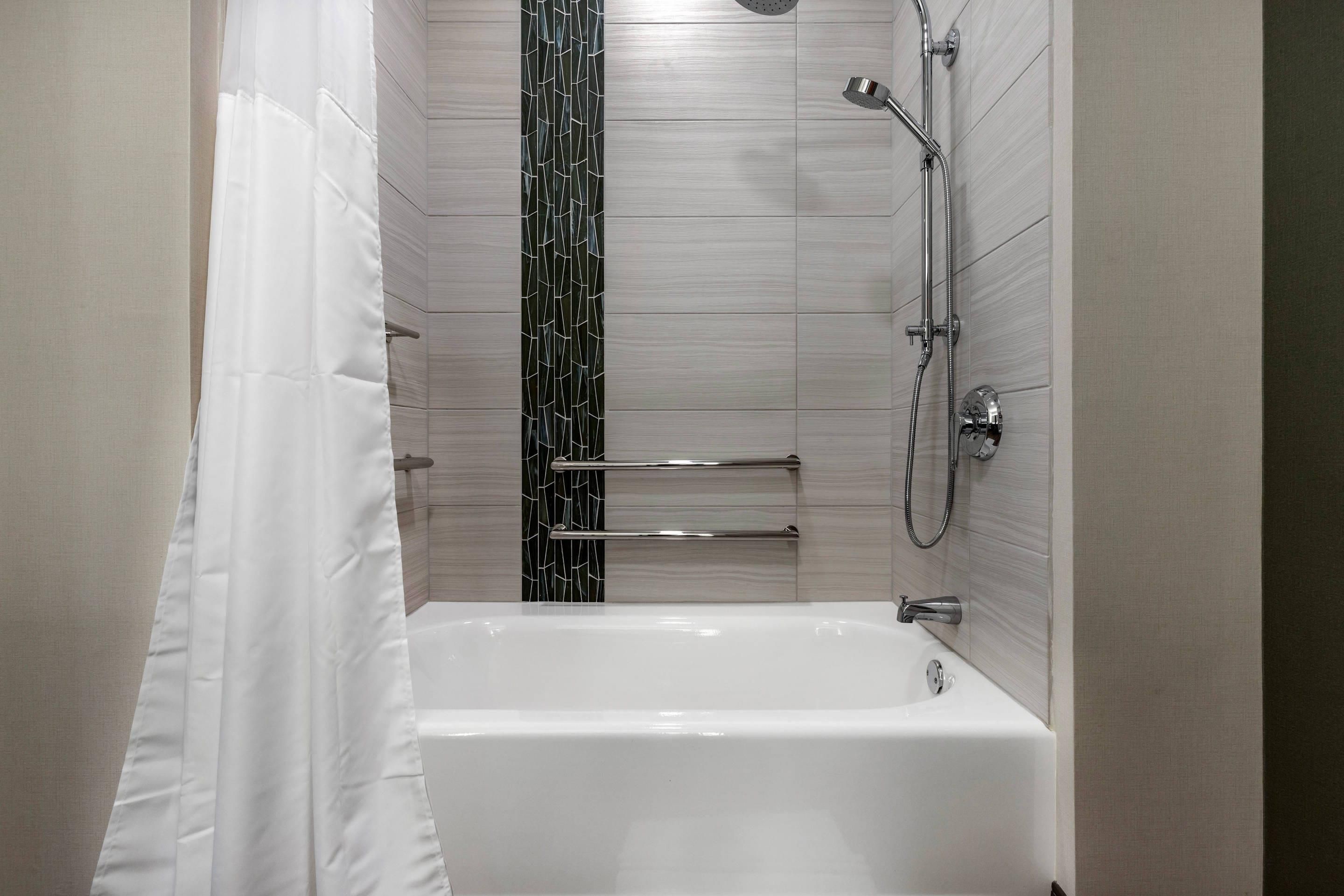 Un baño moderno con una bañera blanca, ducha con cabezal de mano y un perchero de toallas en la pared.