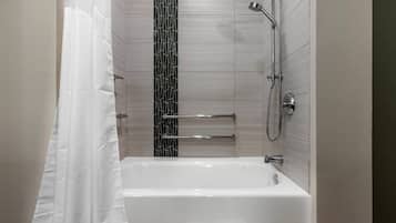 Un baño moderno con una bañera blanca, ducha con cabezal de mano y un perchero de toallas en la pared.