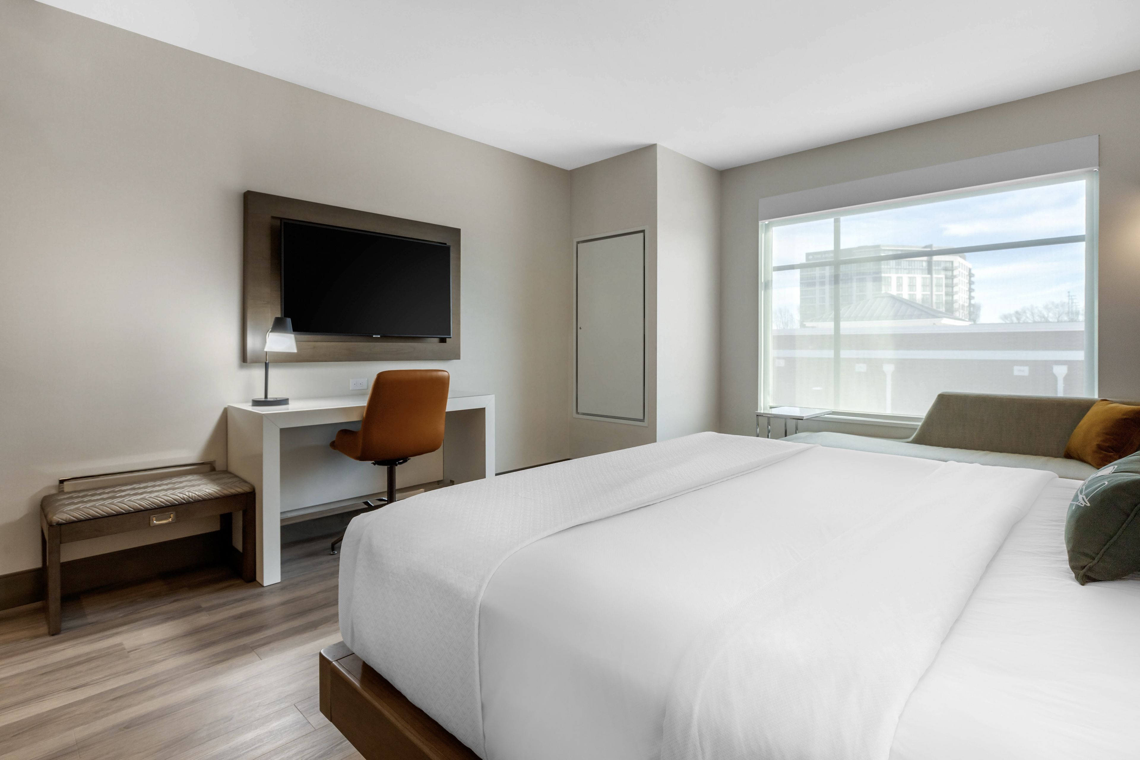 Une chambre d’hôtel équipée d’un lit, d’un bureau, d’une chaise, d’une télévision et d’une fenêtre donnant sur la ville.