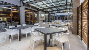 Un patio al aire libre con mesas y sillas, ventanas amplias y techo de cristal.