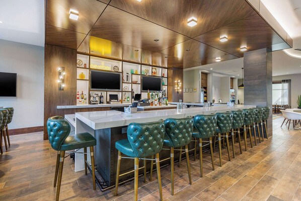Un área de bar moderna con una barra larga, taburetes de bar tapizados en verde y un techo de madera con iluminación empotrada.