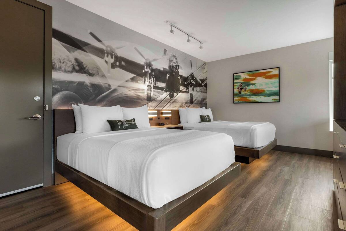 A hotel room with two beds, a large abstract painting on the wall, and a small framed picture.