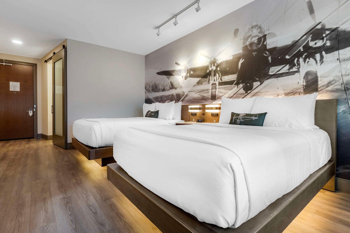 A hotel room with a large bed, a wooden floor, a wall-mounted light fixture, and a door with a handle.