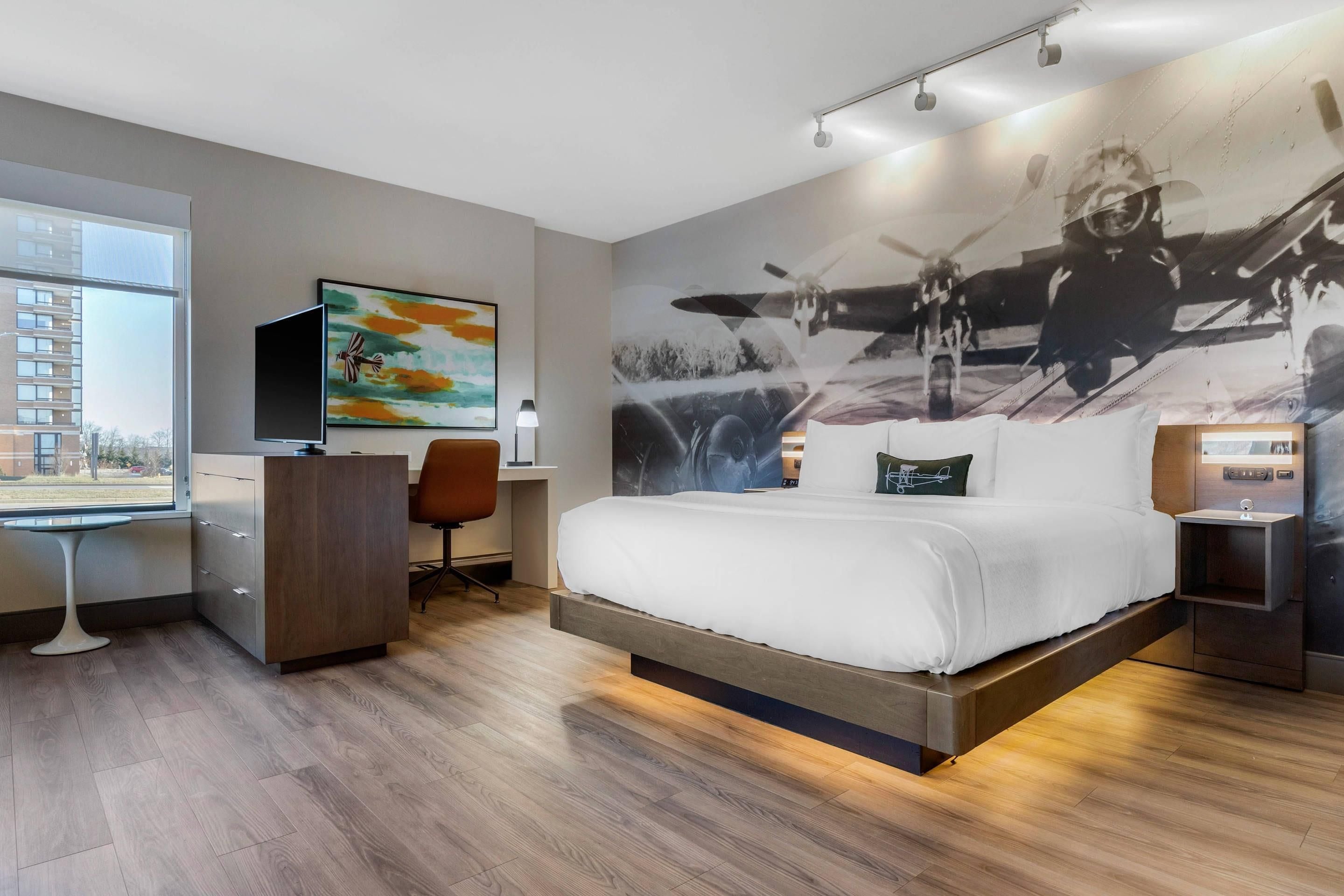 Habitación de hotel moderna con una cama grande, un escritorio, una silla y un ventanal amplio.