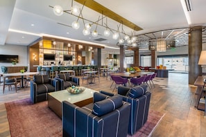 Un moderno vestíbulo de hotel con zona de bar, arreglos para sentarse y una gran pantalla de televisión.