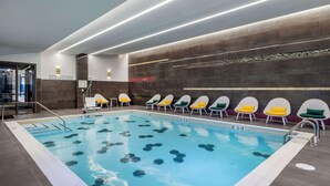 Una piscina con baldosas hexagonales, un vestuario con sillas blancas y amarillas, y una pared con un diseño oscuro.