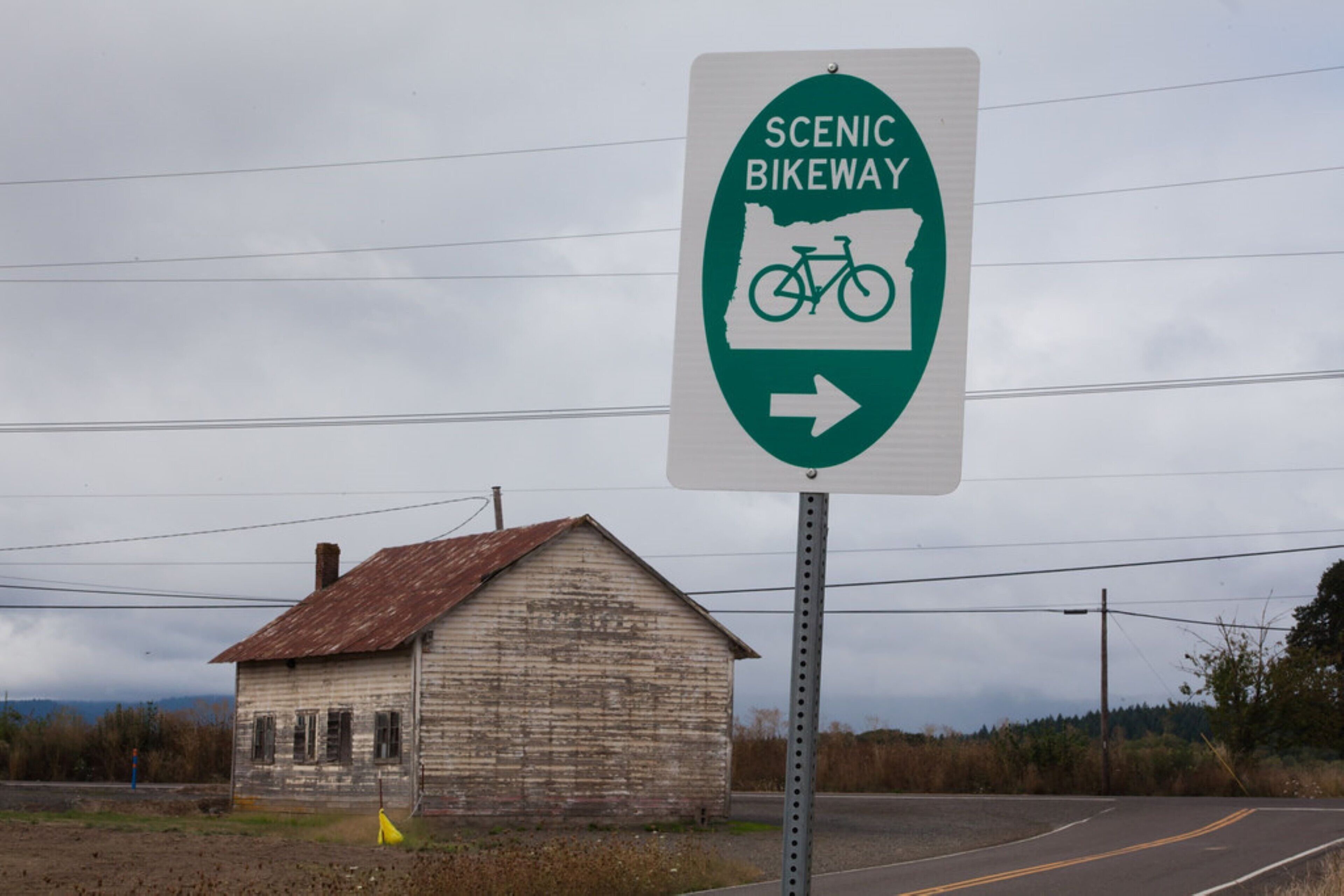 A sign for a scenic bikeway with a rustic wooden building in the background.