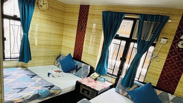 A hotel room with two beds, each with patterned bedding, a clock on the wall, and a window with curtains. - Philippine Hostel (Kowloon)