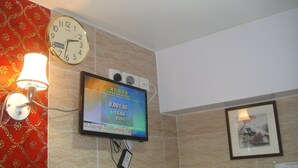 A wall-mounted clock and a digital display in a room with patterned wallpaper and a framed picture. - Philippine Hostel (Kowloon)
