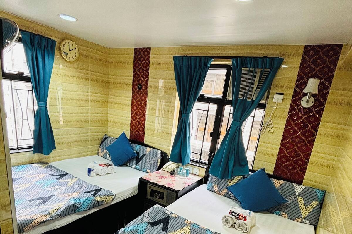 A hotel room with two beds, each with patterned bedding, a clock on the wall, and a window with curtains.