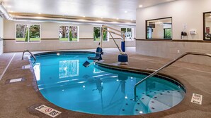 Una piscina interior con un trampolín, una silla de socorrista y un teléfono en la pared.