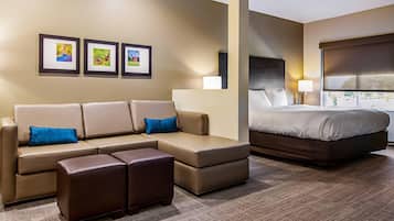 A hotel room with a sofa, ottoman, and a bed. There are framed pictures on the wall.