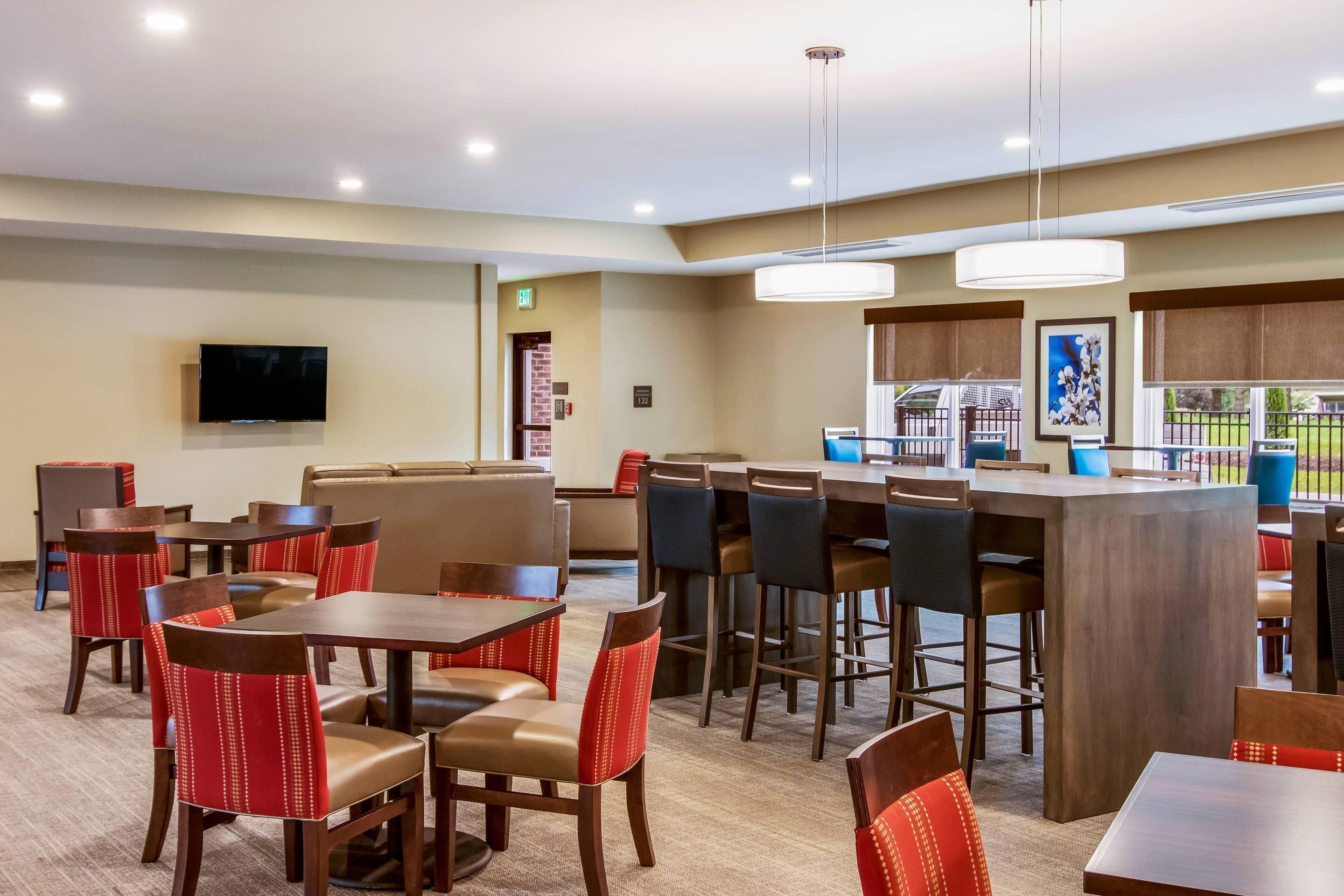 Un hall d’hôtel doté de plusieurs espaces salon, d’un bar et d’un téléviseur fixé au mur.