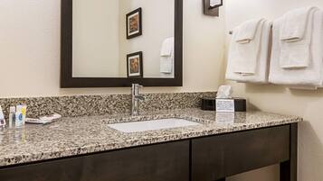 Un baño con encimera de granito, un lavabo, un espejo y un toallero con toallas dobladas.