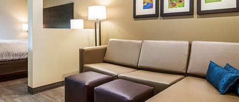 A hotel room with a bed, a sofa, two ottomans, a lamp, and three framed pictures on the wall.