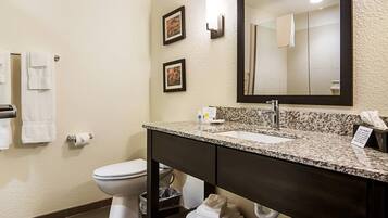 A bathroom with a toilet, sink, and mirror. There are towels on the wall and a trash can.