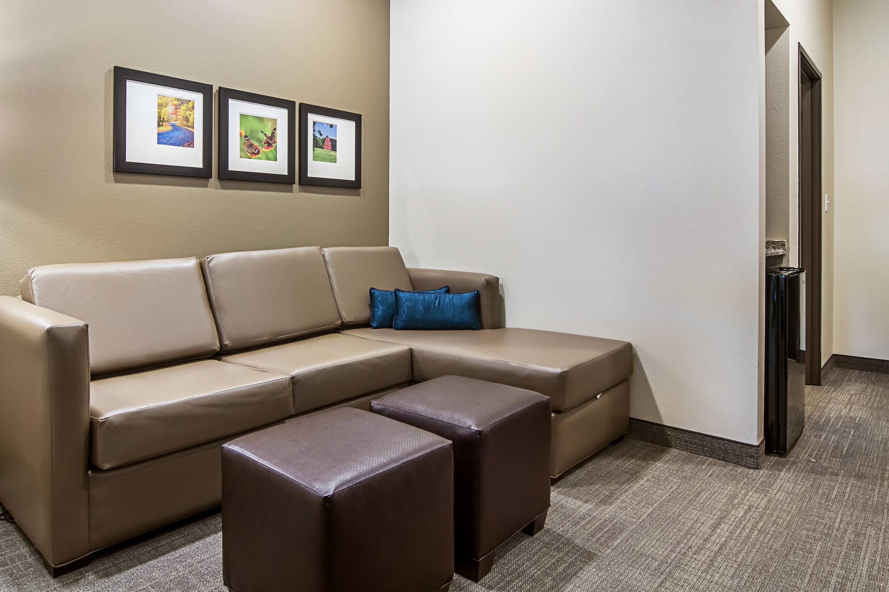 A beige sectional sofa with a blue pillow, two matching ottomans, and three framed pictures on the wall.