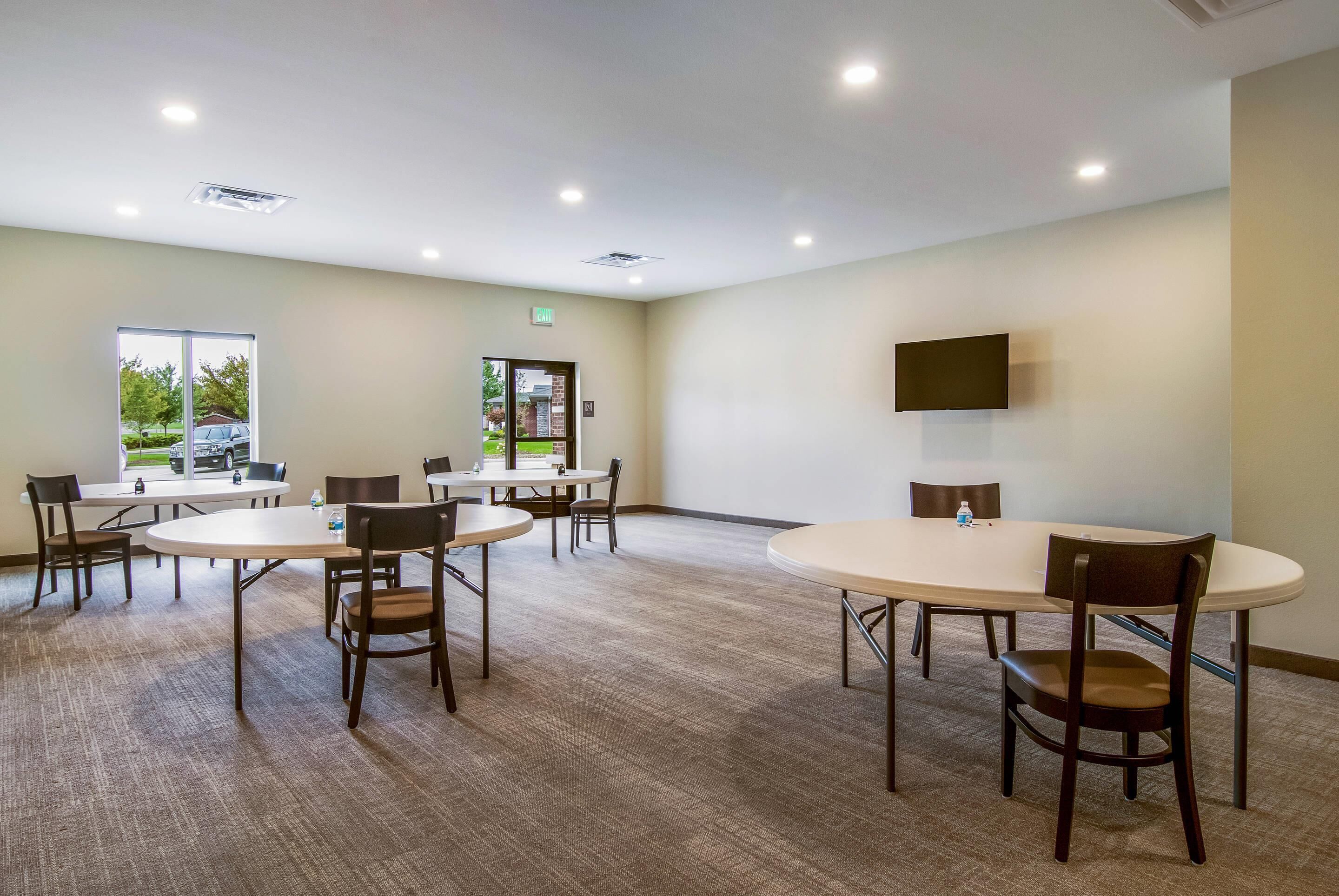 A conference room with round tables and chairs, a mounted TV, and a window with a view of the outdoors.