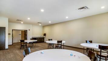 A conference room with four round tables, each with chairs, and a kitchenette area in the background.