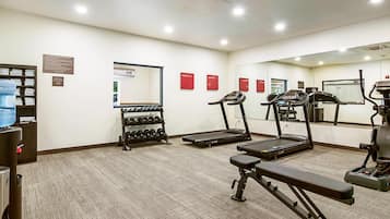 Ett gym med löpband, en bänk och en vattenautomat.