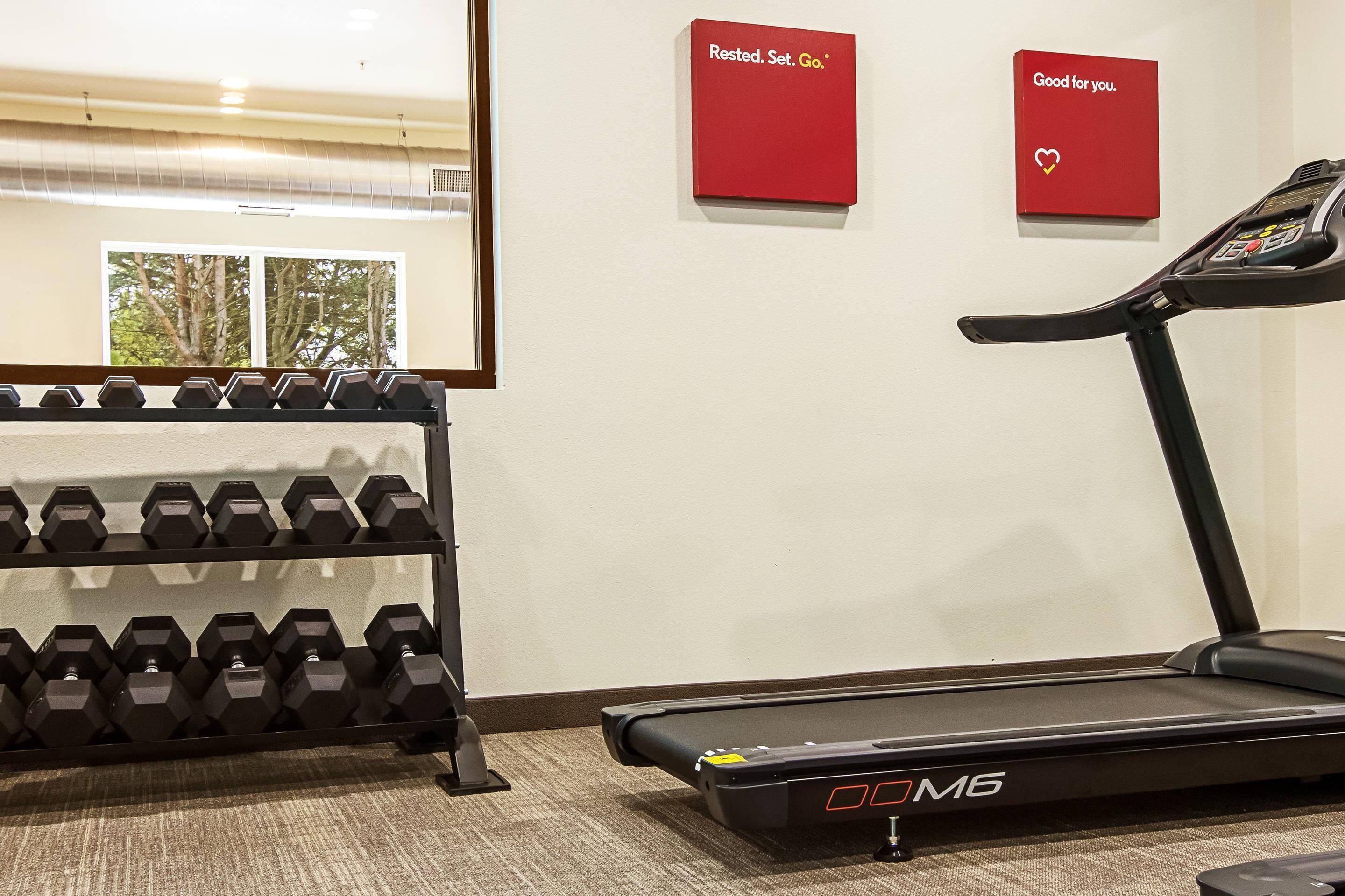 A gym area with a treadmill, dumbbells, and two red signs on the wall.
