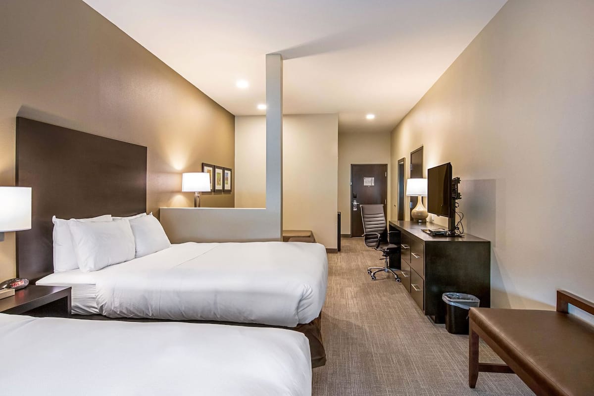 Habitació d'hotel amb dos llits, una taula de treball amb un ordinador, una cadira, una làmpada de taula i un gresol.