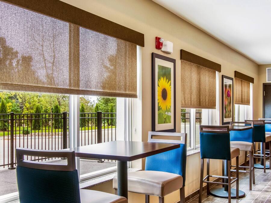 Habitación de hotel con balcón, un ventanal grande con vistas a la vegetación, un cuadro de girasol enmarco y una zona de bar con taburetes y una mesa.