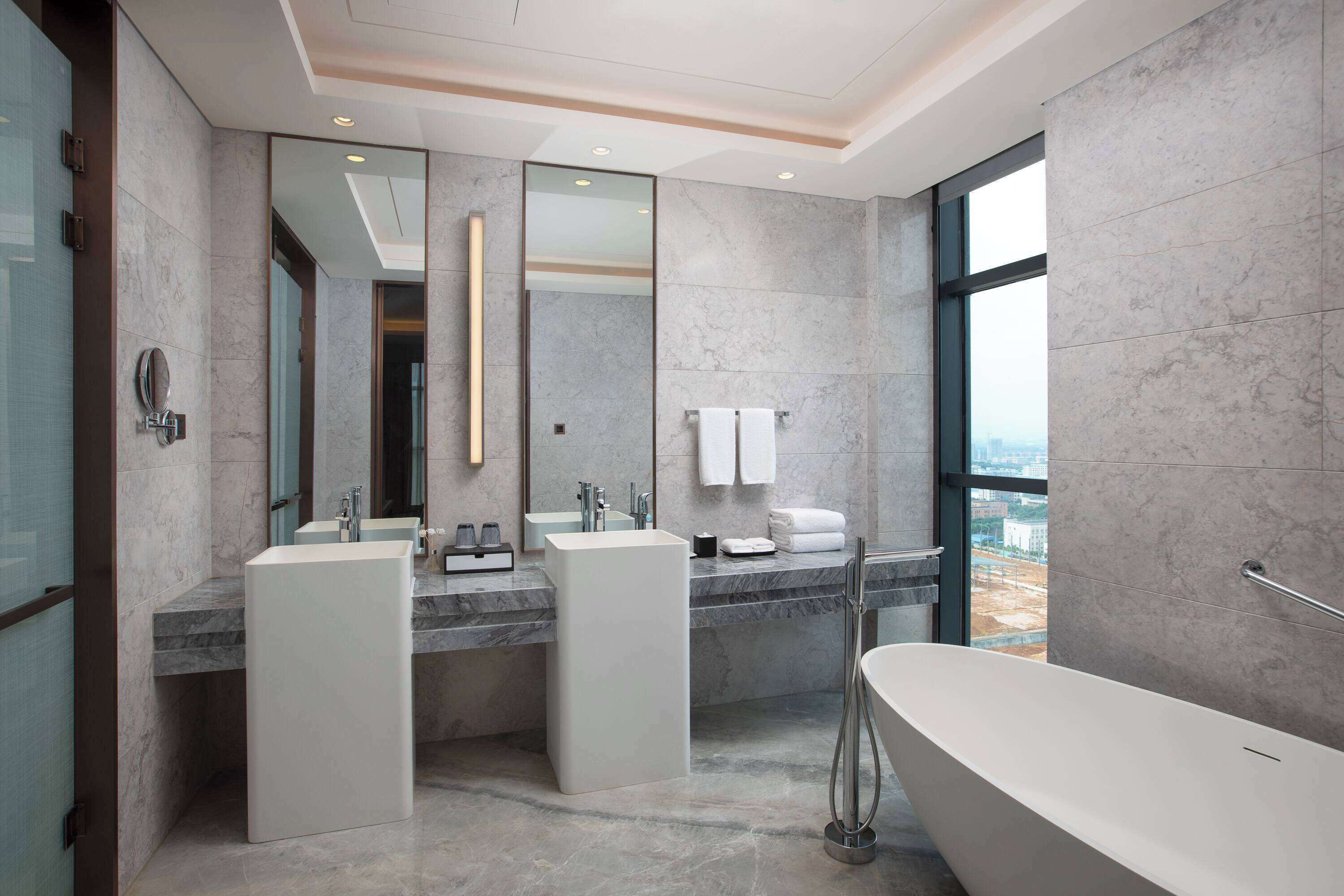 A modern bathroom with two sinks, a large mirror, and a bathtub.