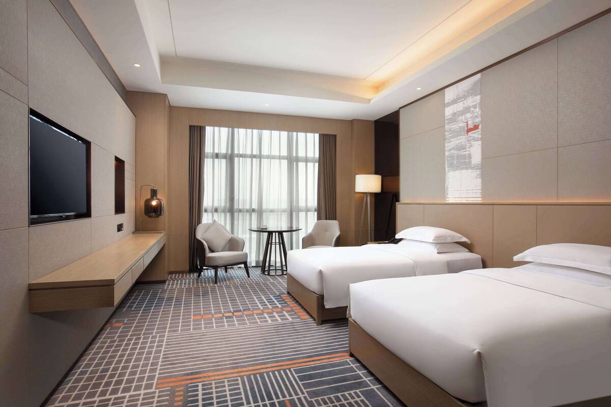 Een hotelkamer met twee bedden, een televisie, een bureau, een stoel en een raam met gordijnen.