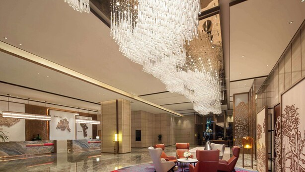 Een moderne lobby met een grote kroonluchter, een receptiebalie van marmer en een comfortabele zithoek.