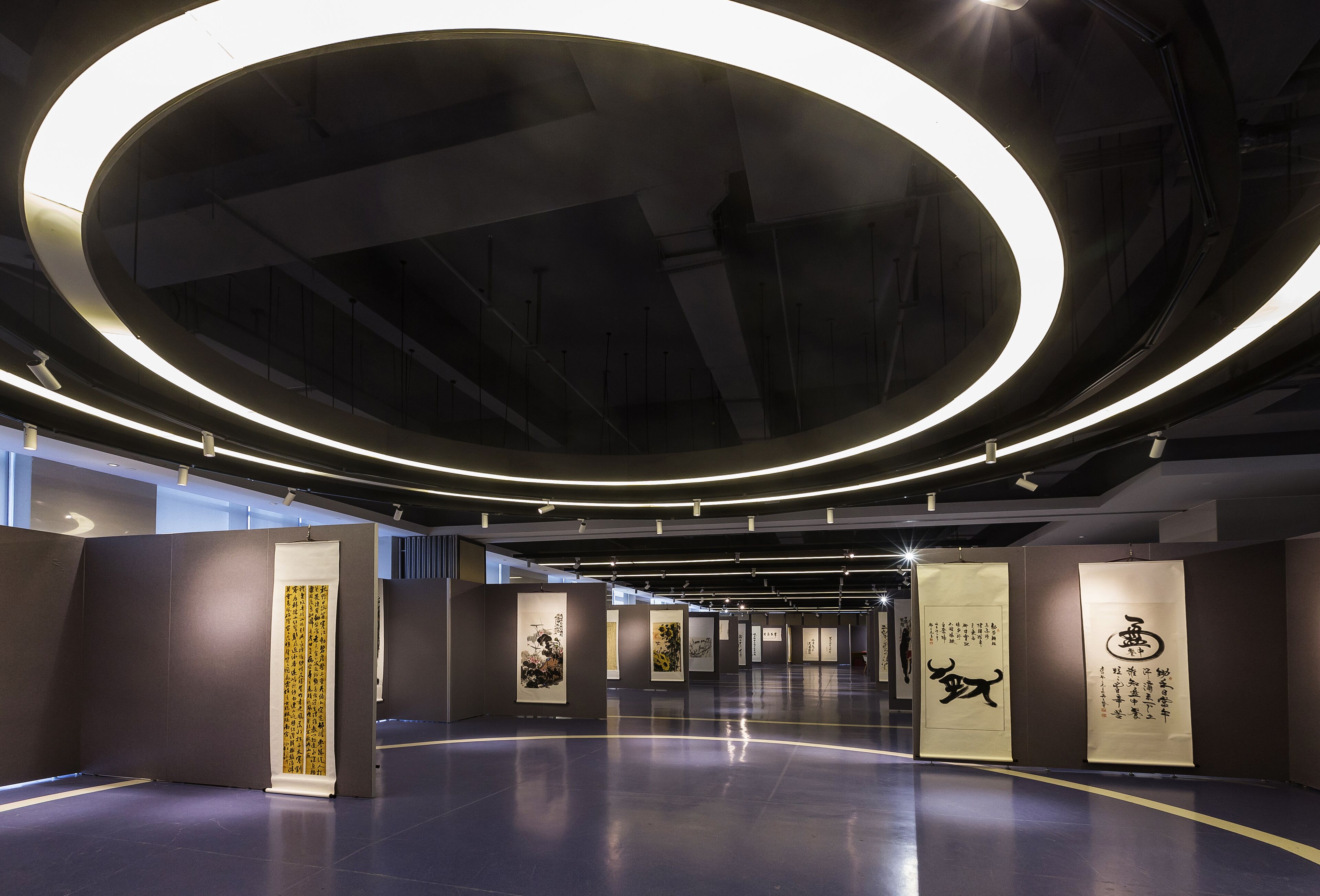 Eine Innenraum-Kunstgalerie mit modernem Design, mit einer zentralen, runden Lichtinstallation und Kunstwerken, die auf Tafeln präsentiert werden.
