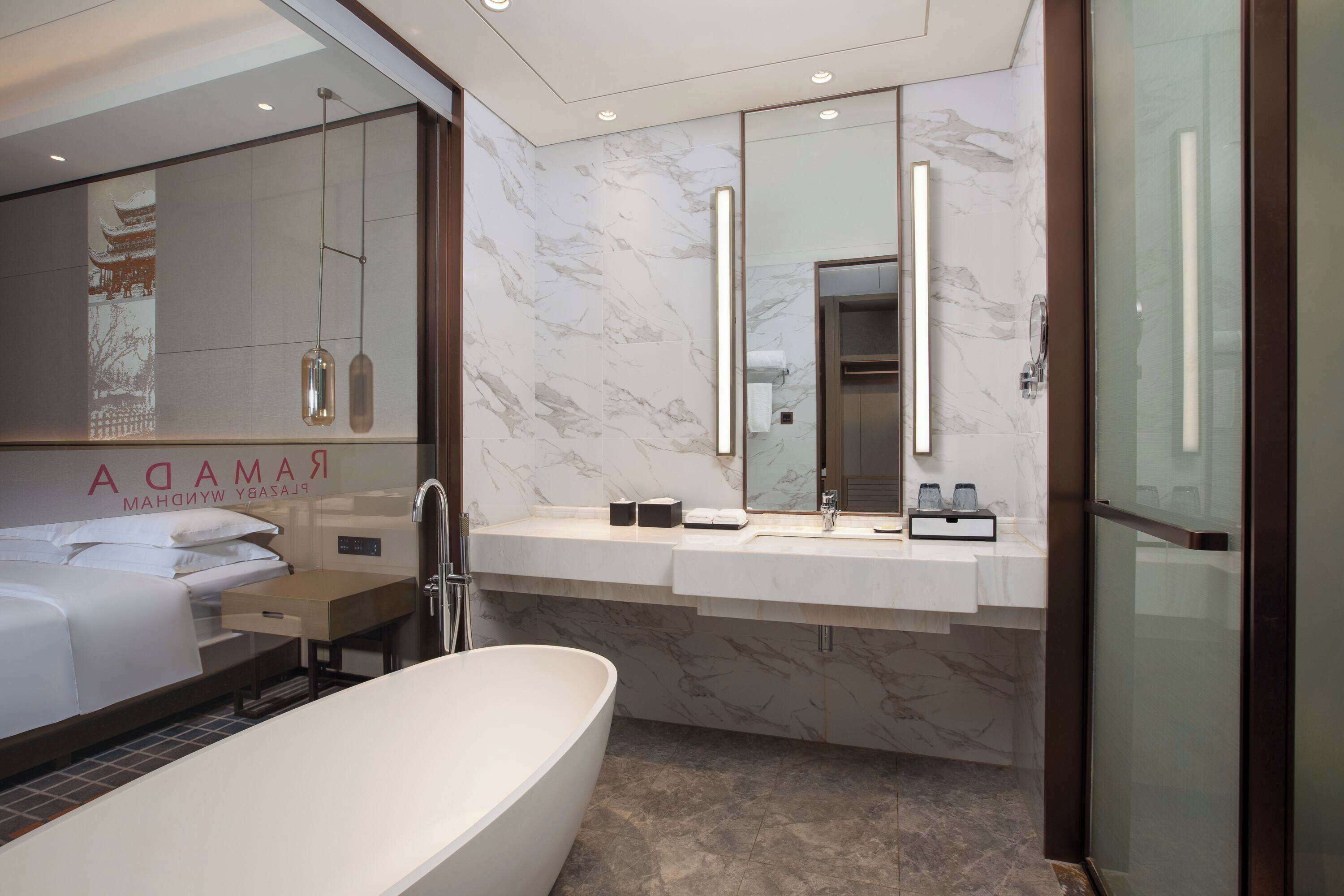 Un baño de hotel moderno con una bañera grande, un tocador con espejo y una cama con cabecero.