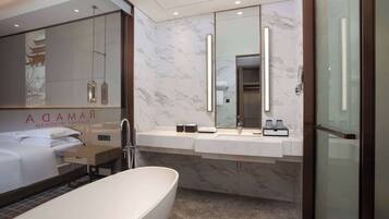 Un baño de hotel moderno con una bañera grande, un tocador con espejo y una cama con cabecero.