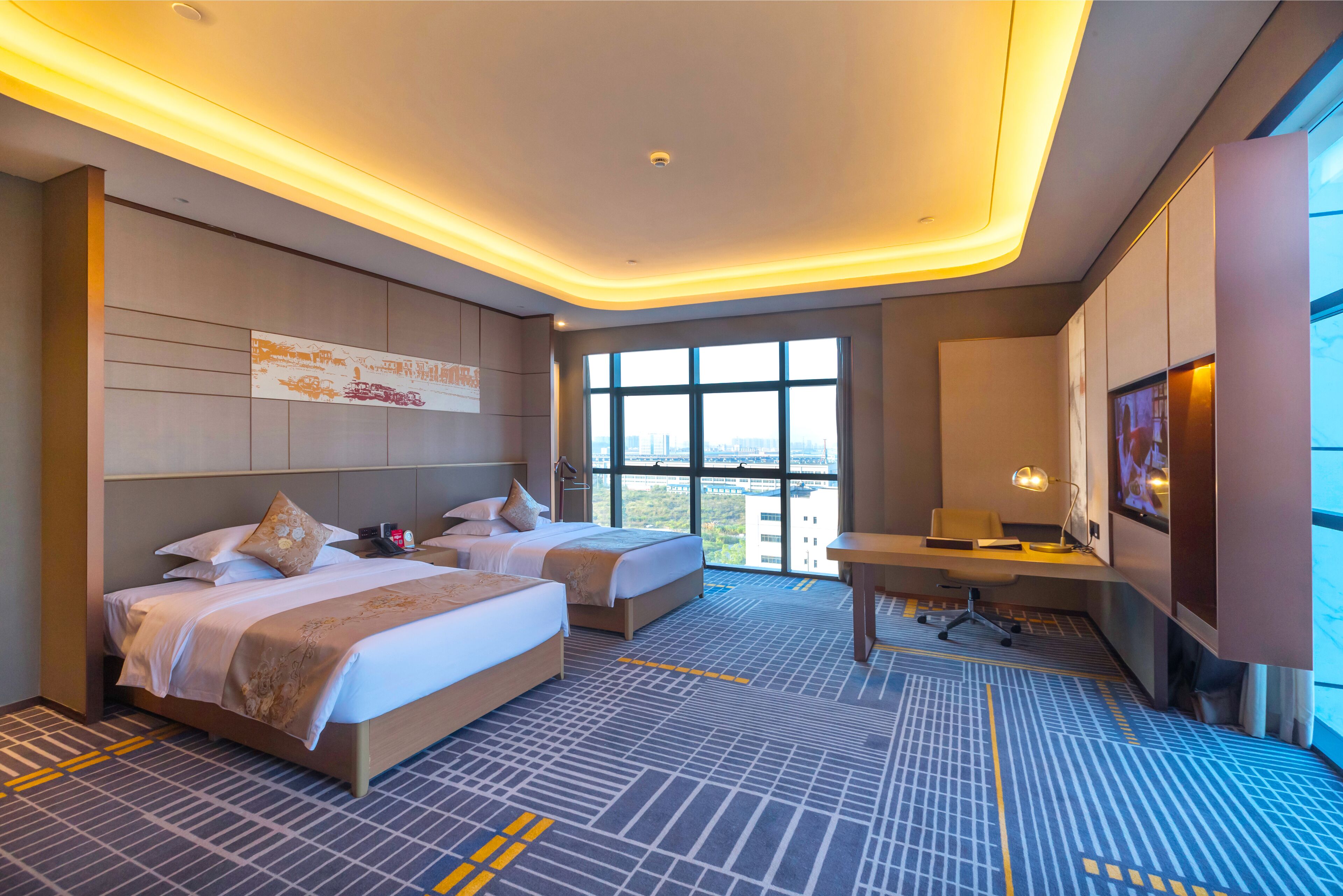 A hotel room with two beds, a desk, and a large window with a city view.