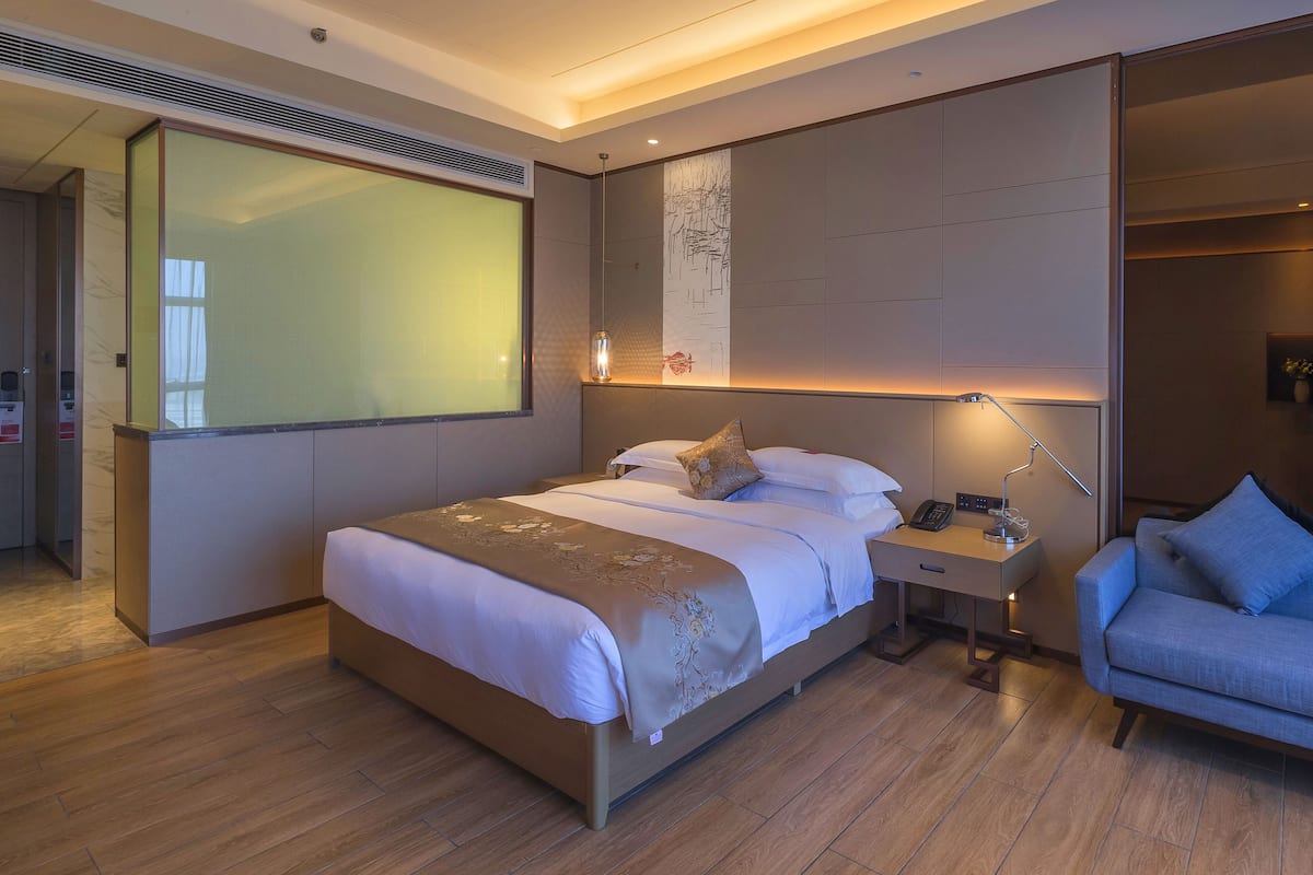 Een moderne hotelkamer met een groot bed, nachtkastje met lamp, een stoel en een groot raam.