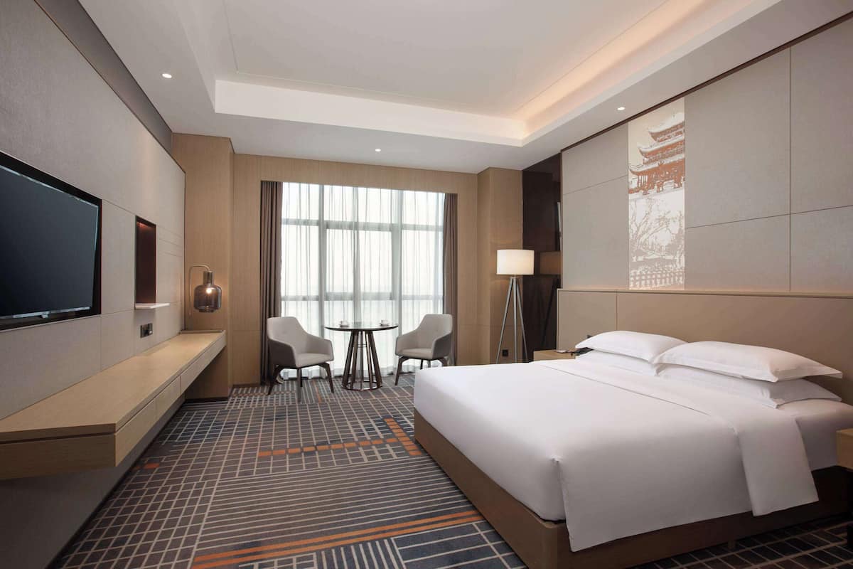 Hotelkamer met een groot bed, een flatscreen televisie, een bureau met stoel en een groot raam met gordijnen.