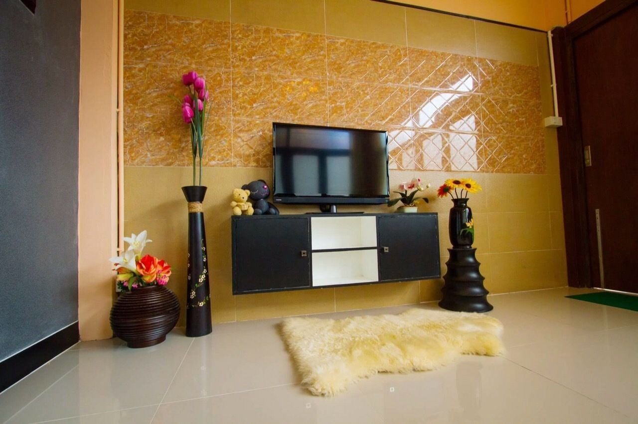 Una sala de estar moderna con un televisor de pantalla plana sobre un mueble negro, un tapete mullido en el suelo y jarrones decorativos con flores.