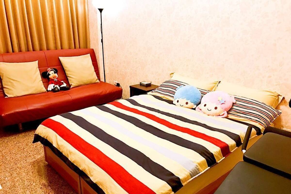 Una habitación de hotel con una cama grande, un sofá rojo y un peluche de Mickey Mouse.
