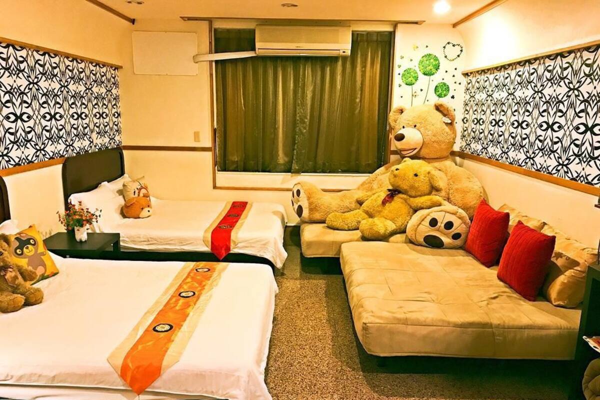 Una habitación de hotel con dos camas, un sofá y un osito de peluche grande.