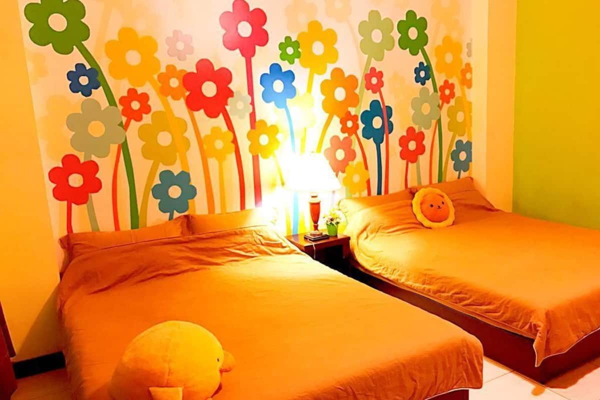 Una habitación con dos camas, una lámpara y una pared decorada con recortes de flores de colores.