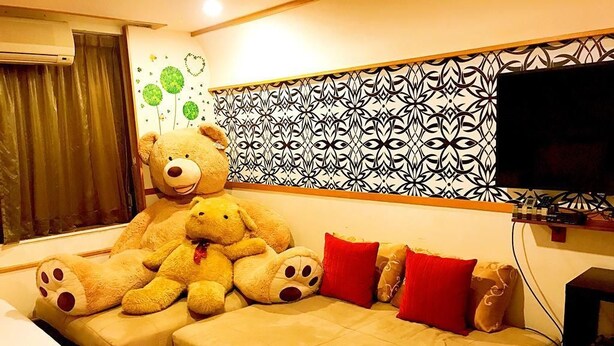 A room with a large sofa, a television, and a teddy bear. - Star B&B (Tainan)
