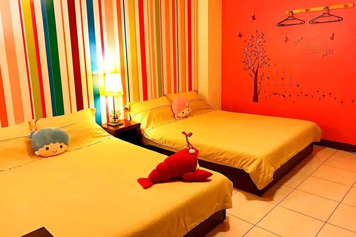Una habitación con dos camas, cortinas a rayas, un mural en la pared y una lámpara.