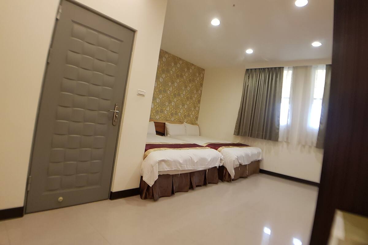 Une chambre d’hôtel avec un grand lit, un plus petit lit, une porte et une fenêtre avec des rideaux.