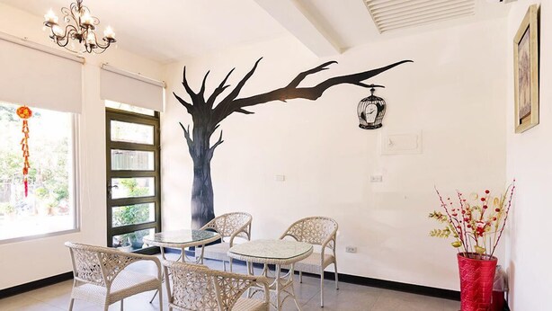 A room with wicker furniture, a large tree mural, a red vase with plants, and a birdcage on the wall. - Tainan Yi Zhan (Tainan)