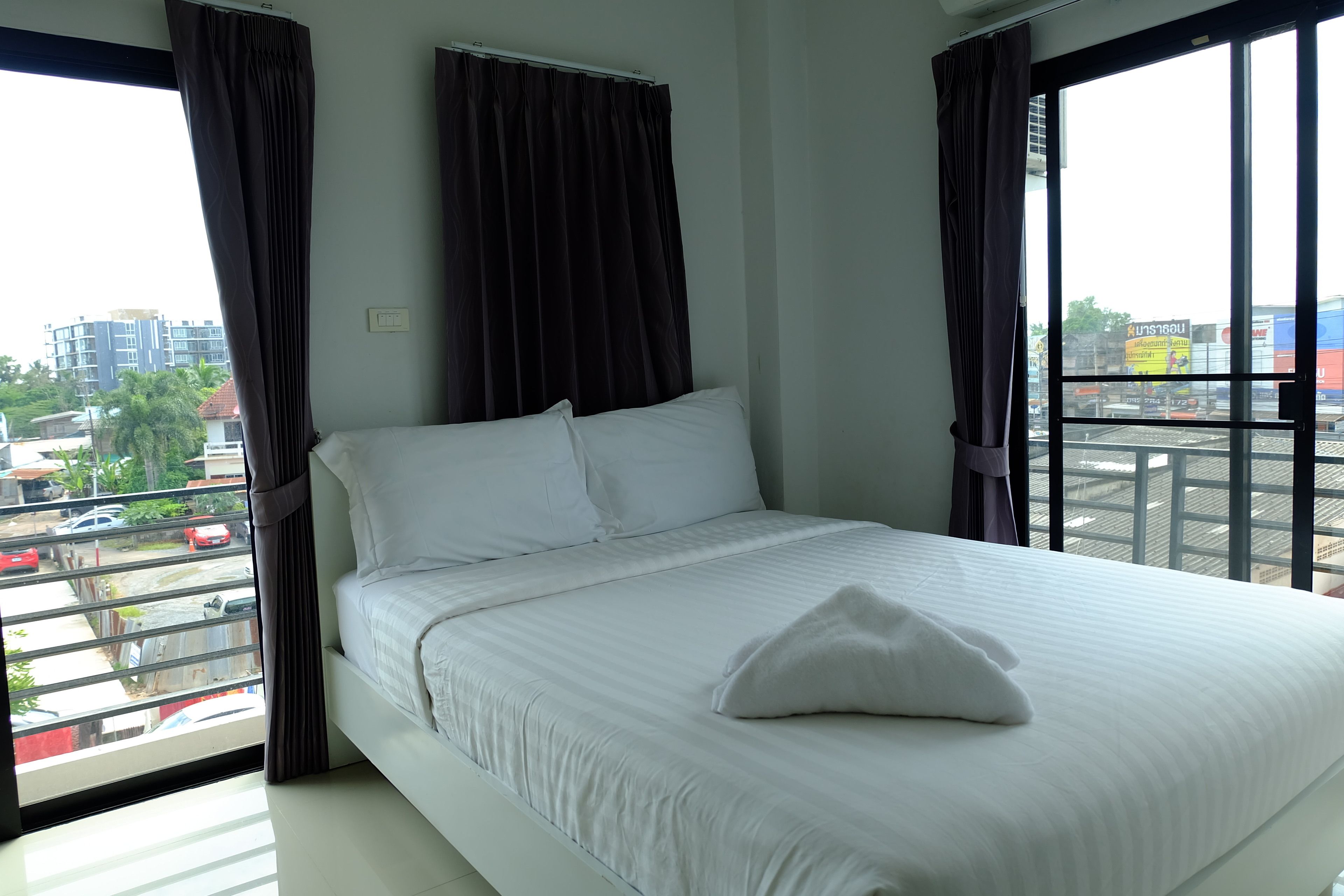A hotel room with a large bed, white bedding, and a view of the city through large windows.