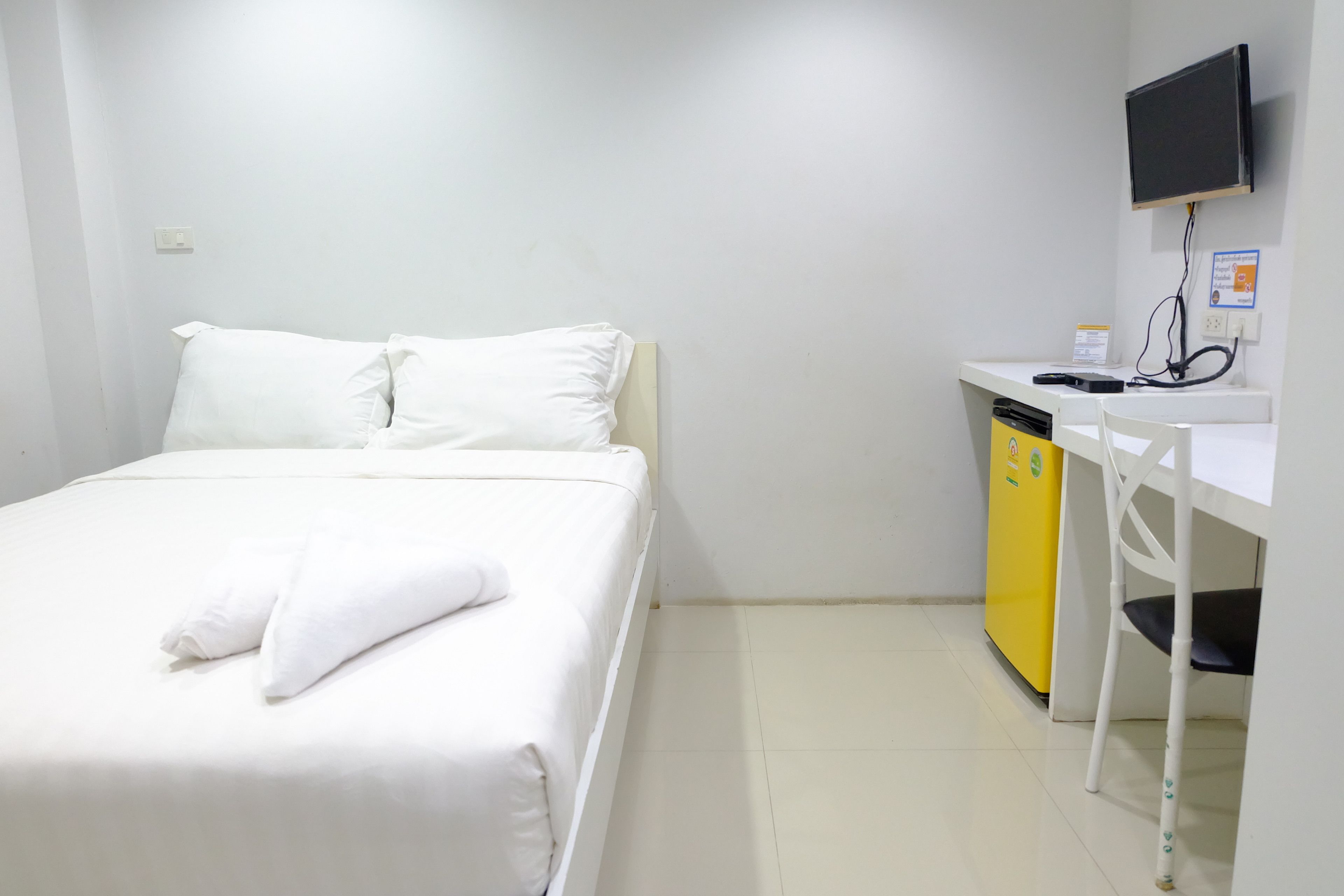 Una habitación de hotel con cama, un escritorio pequeño, televisor y un electrodoméstico amarillo.